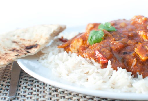 Plate of chicken curry with coriander and naan bread on the side 