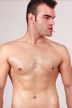 Close up torso look at the bare chest of a fit young man isolated on gray, with lollipop in her mouth