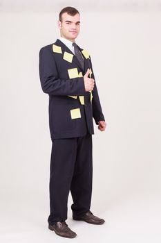 Forgetful businessman with sticky notes covering his suit as reminders, time management and scheduling his tasks giving a thumbs up gesture of approval, full length pose on white