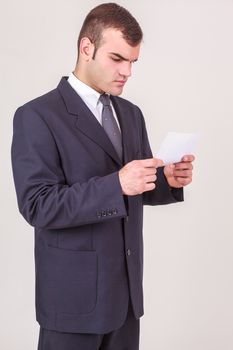 Handsome young businessman in a suit standing frowning as he reads a handheld note, isolated on white