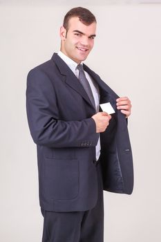 Stylish handsome young businessman smiling at the camera takes a business card from his breast pocket of his jacket, on white, three-quarters