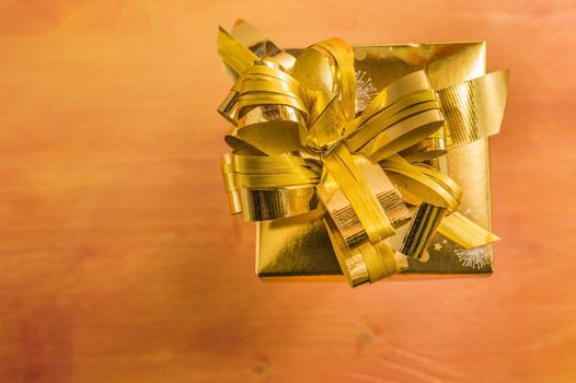 Golden present box with ribbon on wooden background