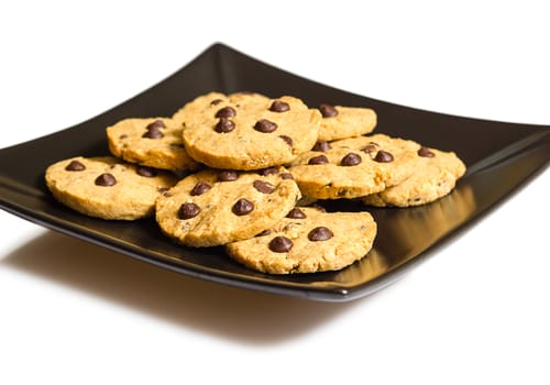 Pile of chocolate chip cookies on a square black plate, isolated on white background