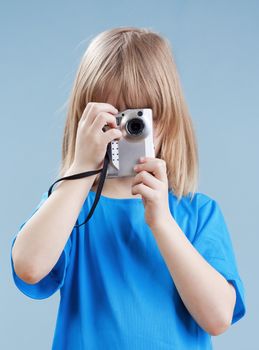 boy with long blond hair taking pictures with digital camera - isolated on blue