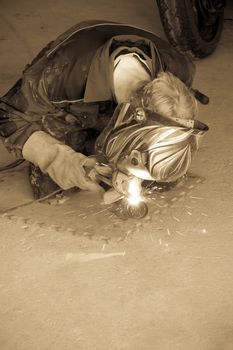 a mechanic welding the exhaust of a motorbike in a garage in sepia