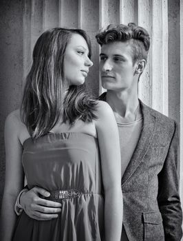 Elegant young couple standing in front of old stone column looking at each other