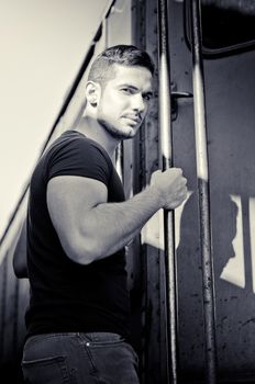 Handsome young man hanging from train handle, looking at camera