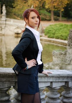 Elegant red-head girl outdoors against stone banister looking at camera