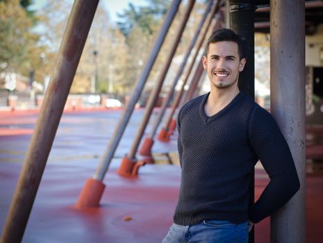 Smiling, friendly young man looking at camera, standing in urban structure