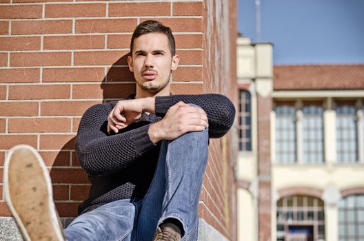 Attractive, confident young man sitting against brick wall outdoors