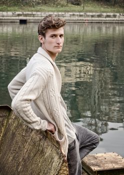 Attractive young man standing against rusty metal next to river waters, looking at camera