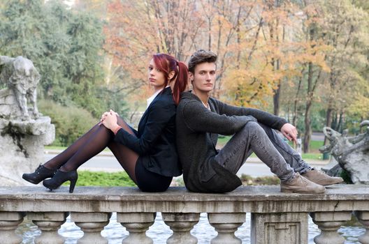 Elegant young couple sitting back to back on old stone balusters, looking at camera