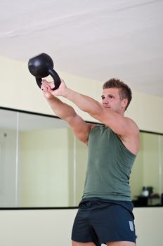 Attractive young athletic man exercising in gym, working out using kettlebell