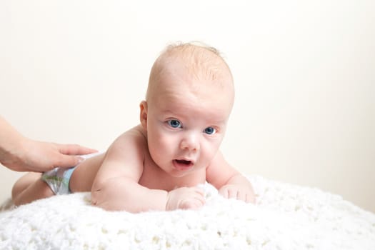 A cute newborn baby boy on a white blanket laying on his belly.