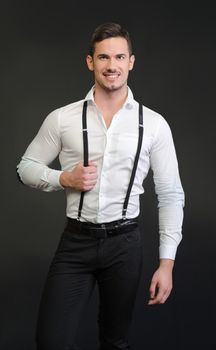 Elegant young man with white shirt and suspenders, on dark background, smiling