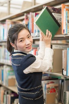 Portrait of young female student taking a green book from a bookshelf in library
