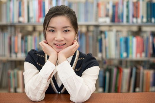 Young student resting on a wooden shelf in front of a bookshelf in library