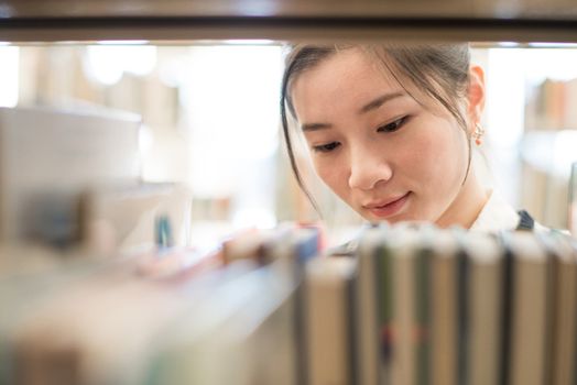 Attractive young woman looking for a book from a bookshelf in library