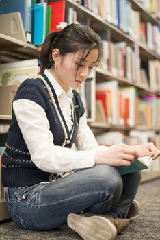 Young attractive woman reading a book while sitting in front of a bookshelf