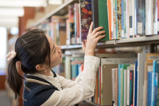 Young female student putting a green book back onto a bookshelf in library