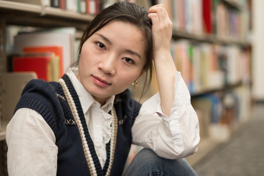 Portrait of stressed young girl next to a bookshelf supporting head with one arm