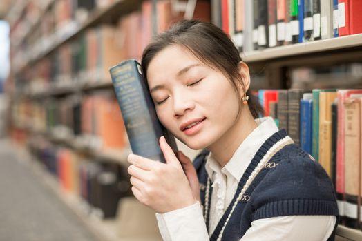 Young girl sitting in front of a bookshelf resting head on a thick old book