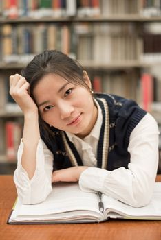 Pretty female student sitting at a desk with a open book studying in the library