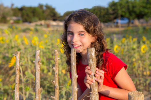 Smiling farmer girl with sunflowers field holding fence door in Mediterranean