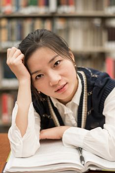 Pretty female student sitting at a desk with a open book studying in the library