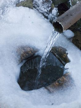 Running spring water from metal tube in the village, winter