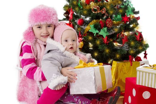 Two sisters sitting with gifts under Christmas tree on white