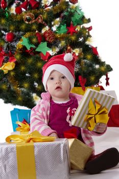 Cute little girl in Santa hat sitting under Christmas tree over white