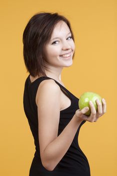 teenage girl holding a green apple smiling - isolated on yellow