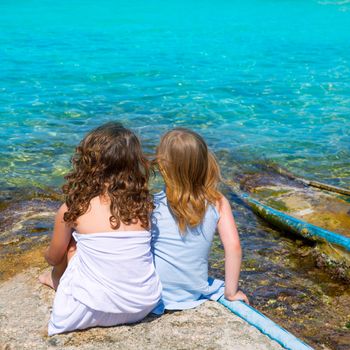 Blond and brunette kid sister girls sitting on beach port in Formentera summer vacation