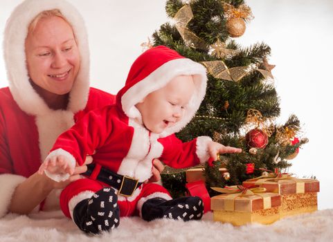 Christmas baby and mom open gifts under the fir tree