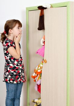 shocked little girl looking into a messy closet 