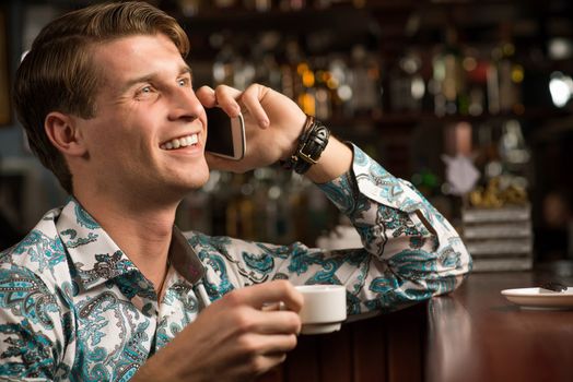 young man at the bar on the phone and drinking coffee