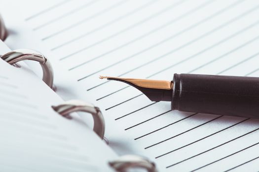 Metal feather pen on the ruled paper in the notebook