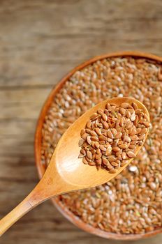 close up of flax seeds and wooden spoon on wood background; dietary supplement