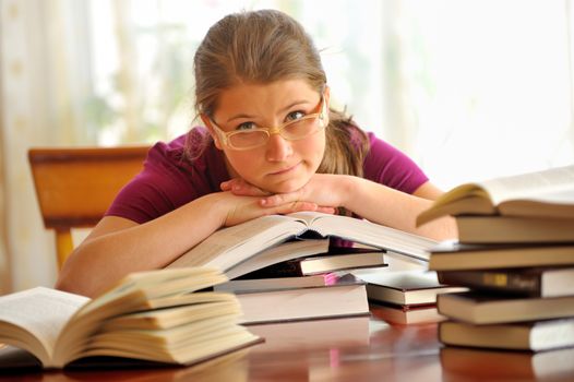Teen girl learning at the desk, sitting on books