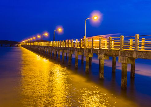 Pier at night with yellow lights on a background of blue sky stretching into the sea