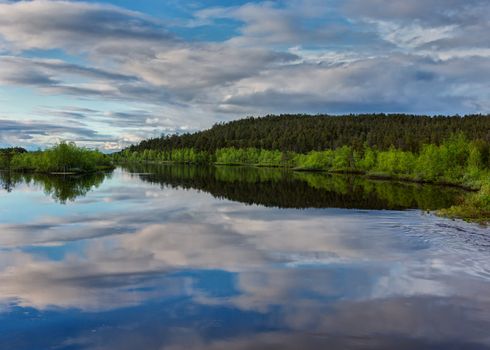 Plenty of water and forests under blue skies filled with all kind of clouds, all mirrored in lake.