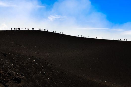 Group of trekkers hiking on a volcano hill with blue sky background