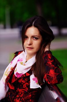 Attractive girl in a red coat sitting on a bench in spring park.