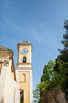 A yellow stucco clock tower into blue sky in Eze, France