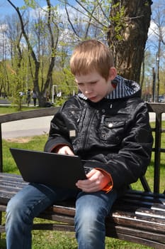 the teenager with the laptop sits on a bench in park