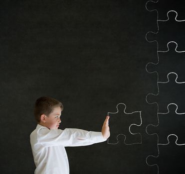 Boy pushing puzzle piece into place on blackboard background