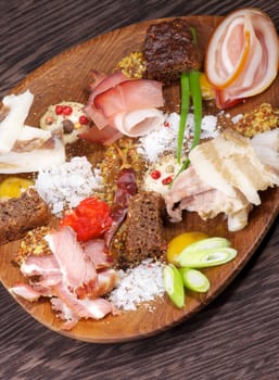 Wooden Plate with Various Smoked, Boiled and Uncooked Ham, Mustard, Salt, Brown Bread and Spices on Dark Wooden background