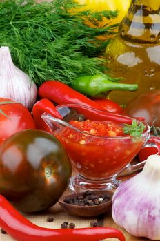 Arrangement of Bruschetta Sauce in Glass Gravy Boat with Black Tomatoes, Garlic, Chili Peppers and Olive Oil in Glass Bottle closeup on Wooden background