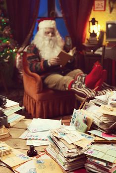 The messy desk of Santa Claus, he reading a book on background